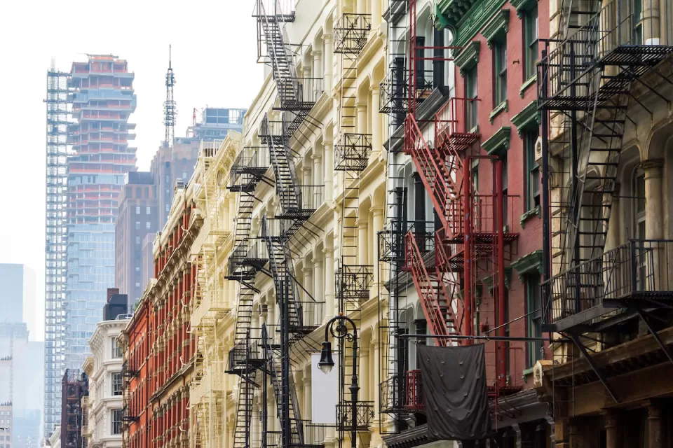 Brick New York City apartment buildings with fire escapes and high-rise under construction in background.
